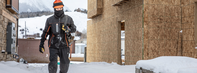 Construction worker wearing cold weather workwear on snowy construction site.