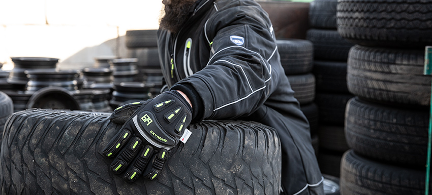 Person wearing impact protection insulated work gloves moves a large tire.