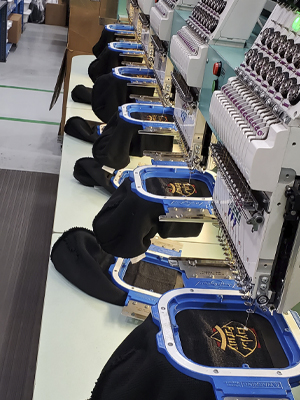 : Row of embroidery machines embroidering hats. RefrigiWear has an in-house embroidery team to personalize your gear.